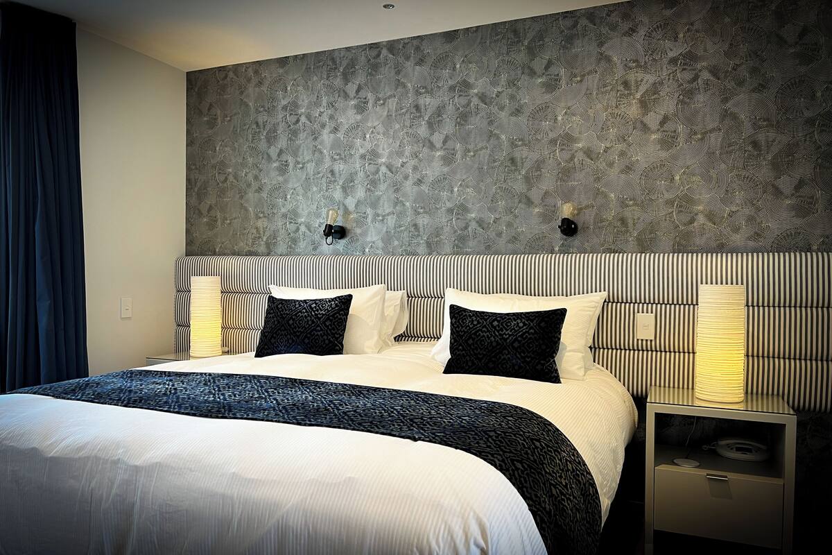 A modern hotel room with a large bed, striped headboard, and a patterned wall.