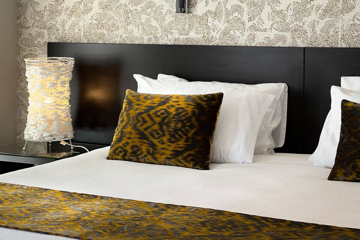 A neatly made bed with white and patterned pillows, a textured throw blanket, and a decorative lamp on a bedside table.