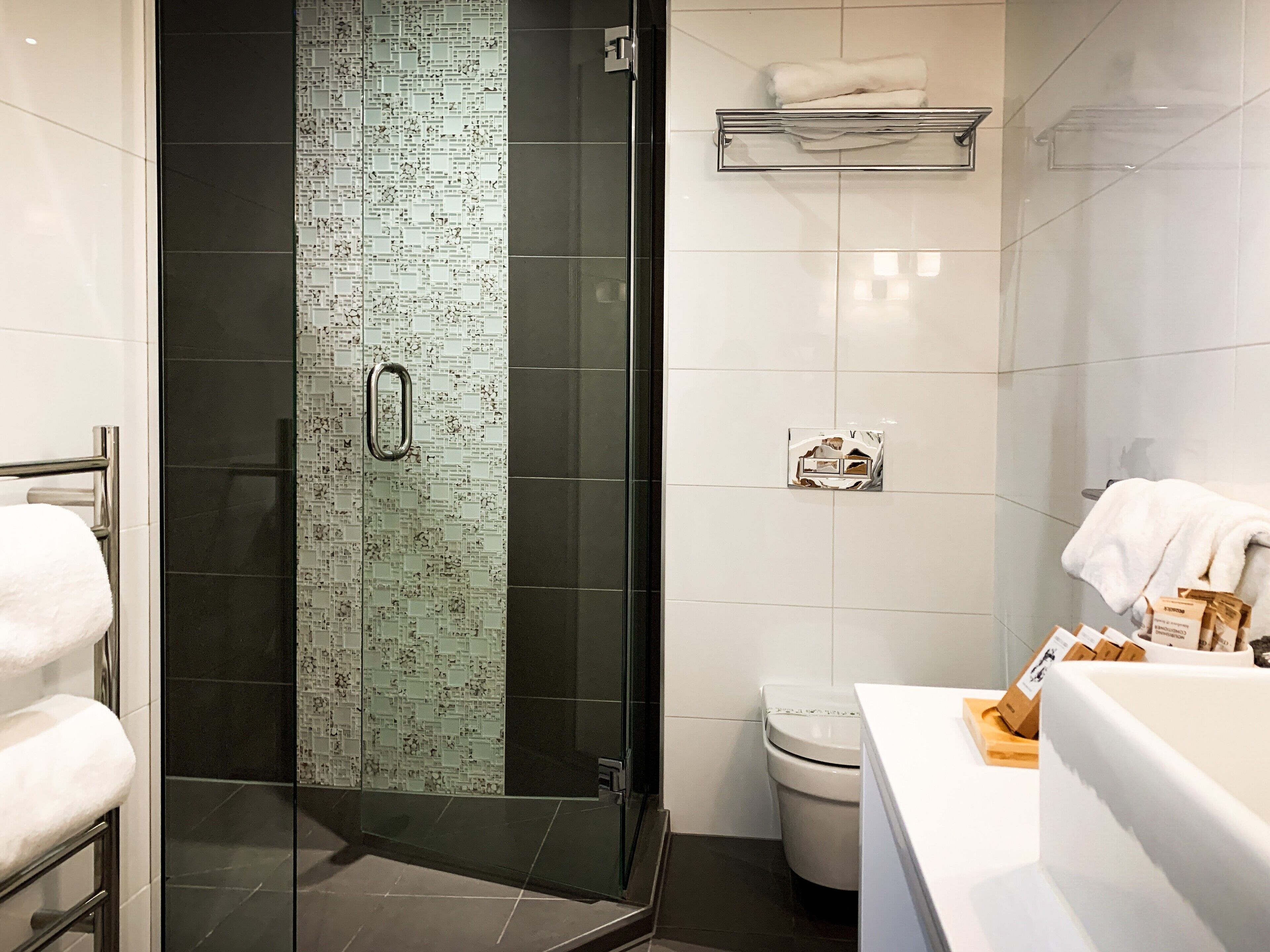 Une salle de bain moderne avec une douche à parois de verre, des toilettes blanches et un lavabo blanc doté d’un porte-serviettes.