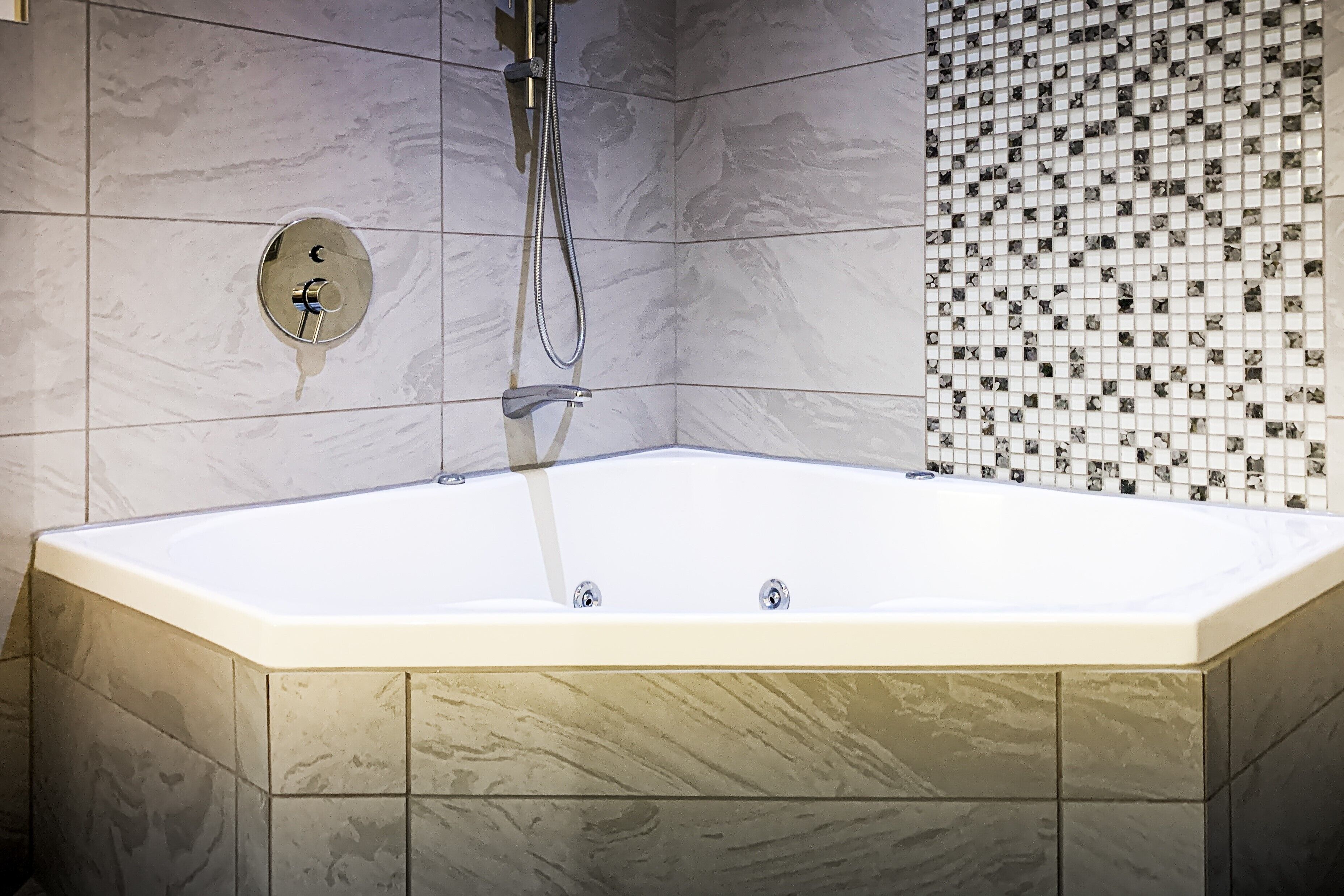 A corner bathtub with a showerhead, surrounded by marble tiles.