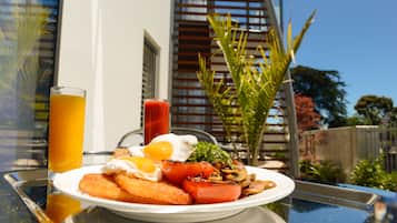 Un plato de desayuno con huevos, tomates y tostadas sobre una mesa frente a un edificio, con vistas a árboles y una cerca.