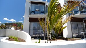 A modern two-story building with a balcony, outdoor seating, and a landscaped garden area.