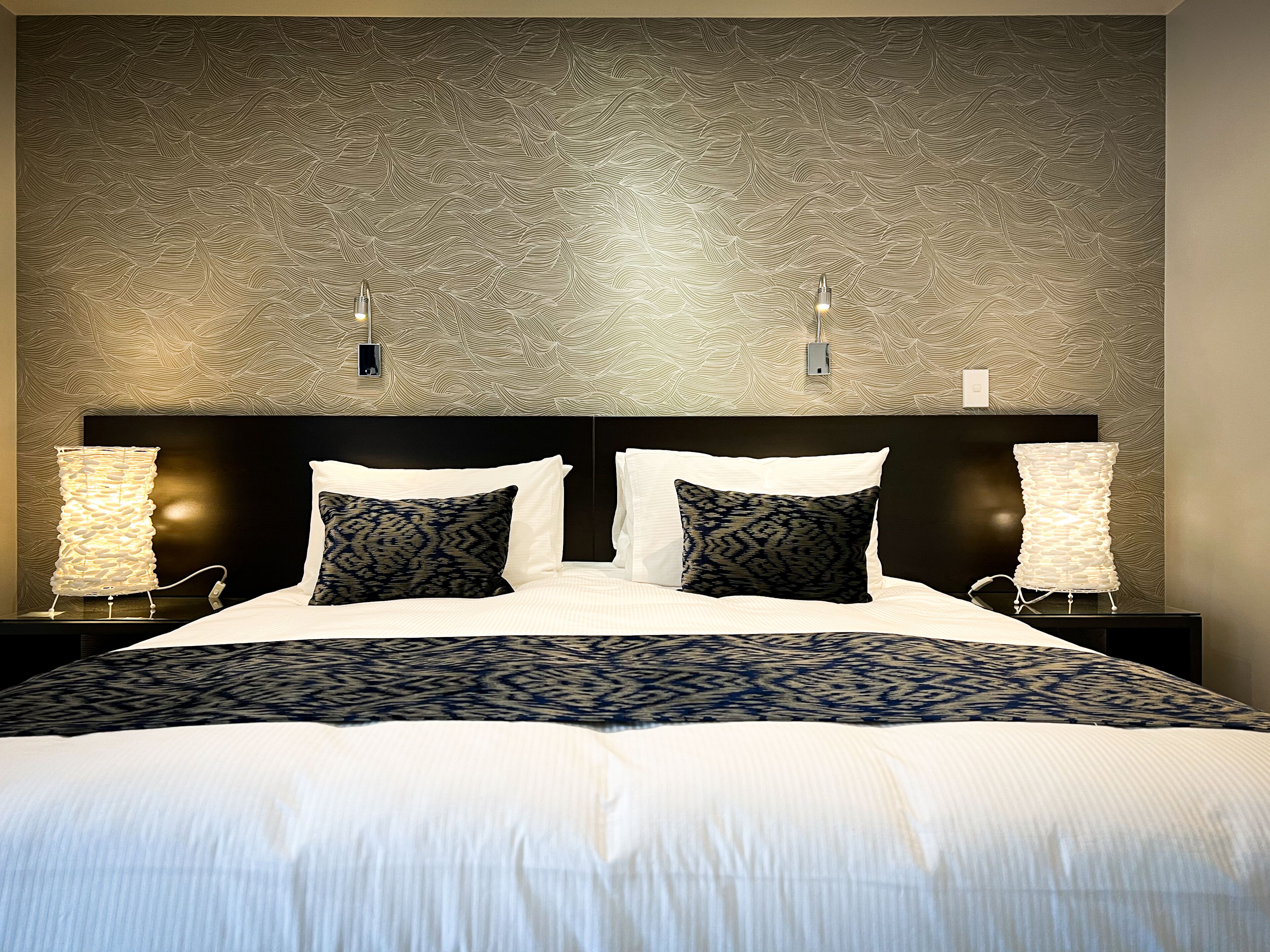 A neatly made bed with a patterned bedspread, two bedside lamps, and a textured wall behind.