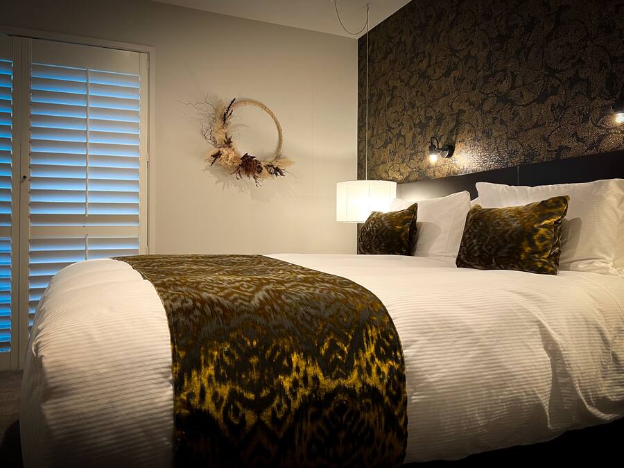 A neatly made bed with a patterned throw, a wall-mounted lamp, and a decorative wall piece.
