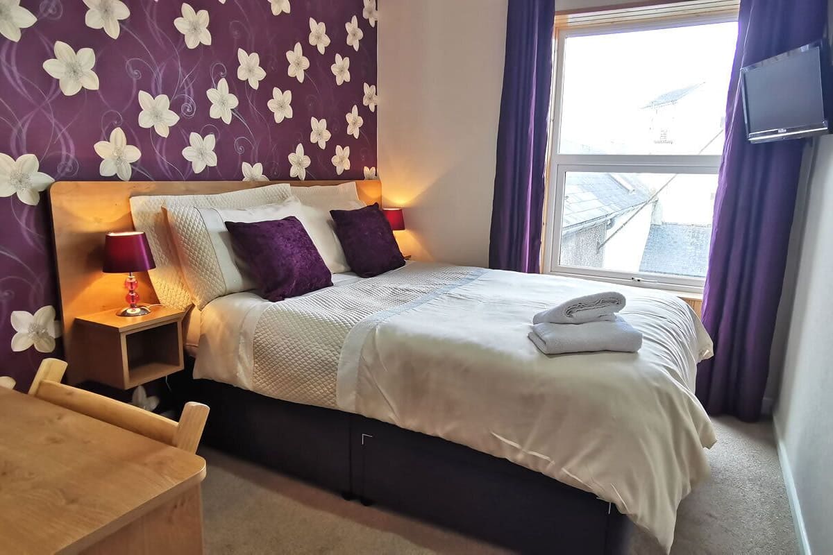 A hotel room with a bed, a nightstand, a TV, and a window with curtains.