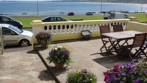 A patio area with outdoor seating, a view of the sea, and parked cars.