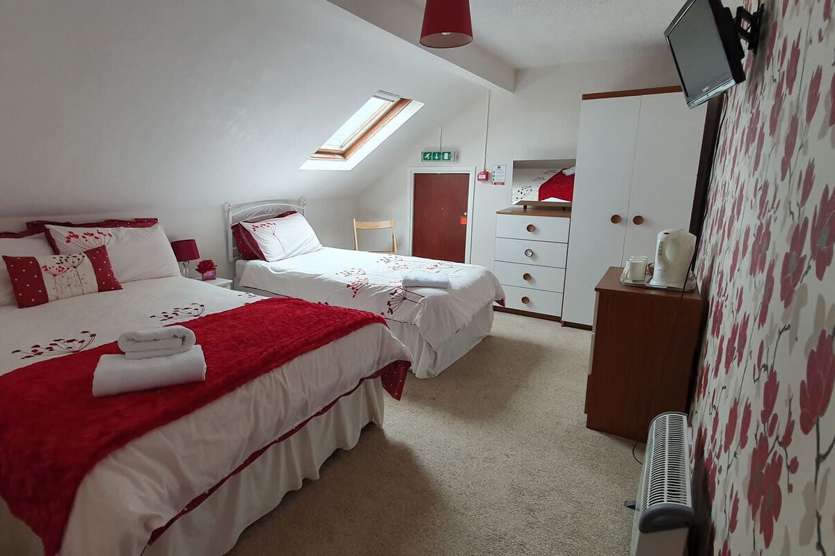 A hotel room with two beds, a TV, a wardrobe, and a desk.