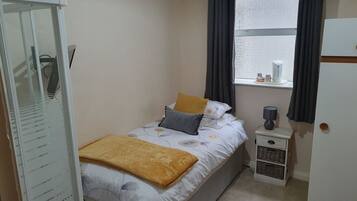 A small, neatly arranged bedroom with a bed, a nightstand, a window with curtains, and a wardrobe.