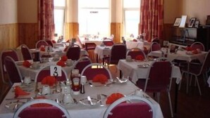 A dining area with tables set for service, numbered seating, and a view of the sea through large windows.