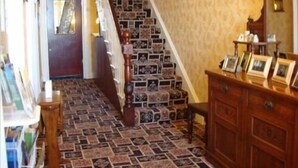 A staircase with a patterned carpet, a wooden staircase railing, and a wooden dresser with framed pictures.