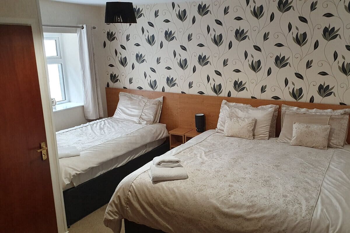 A hotel room with two beds, a patterned wallpaper, and a window with curtains.