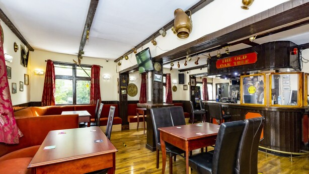 A traditional inn with wooden floors, red cushioned seating, and a bar area. - Old Oak Tree Inn (Southall)