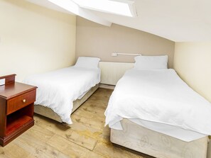 A small, clean room with two single beds, a wooden nightstand, and a skylight. - Old Oak Tree Inn (Southall)