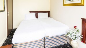 A neatly made bed with white linens, a wooden headboard, and striped bedding at the foot of the bed. - Old Oak Tree Inn (Southall)