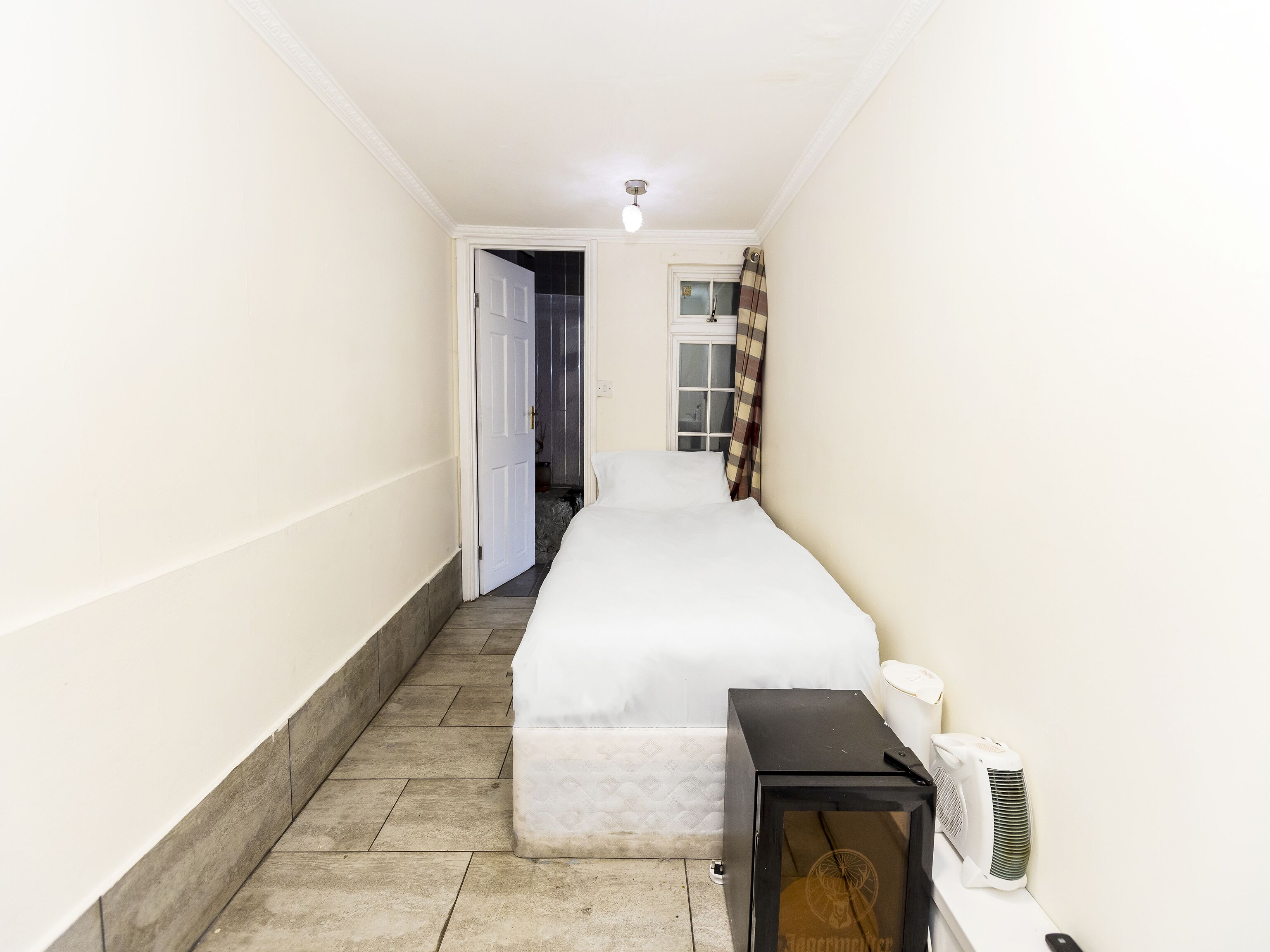A narrow hallway leading to a bedroom with a bed, a bedside table, and a wall-mounted air conditioner.