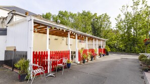 A covered outdoor seating area with red chairs and tables, surrounded by potted plants and a red picket fence. - Old Oak Tree Inn (Southall)