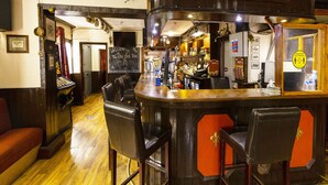 A bar area with a sign reading "The Old Oak Tree," bar stools, a cash register, and a wooden floor. - Old Oak Tree Inn (Southall)