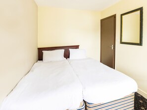 A double bed with white linens, a wooden headboard, and a striped rug at the foot of the bed. - Old Oak Tree Inn (Southall)