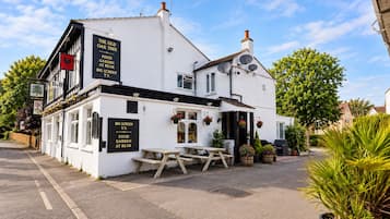 A white building with a sign indicating a pub named 'The Old Oak Tree' offering food, a garden, and a big screen TV.