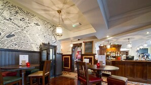 A restaurant with wooden tables and chairs, a bar area, and a wall with a map. - The Rose and Crown (York)