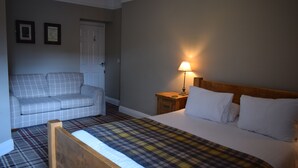 A hotel room with a bed, a sofa, a nightstand with a lamp, and a door. - The Rose and Crown (York)