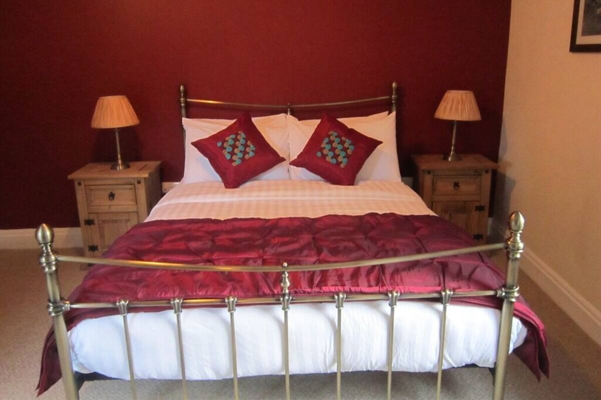 Uma cama com estrutura de metal, duas mesas de cabeceira e uma parede vermelha.