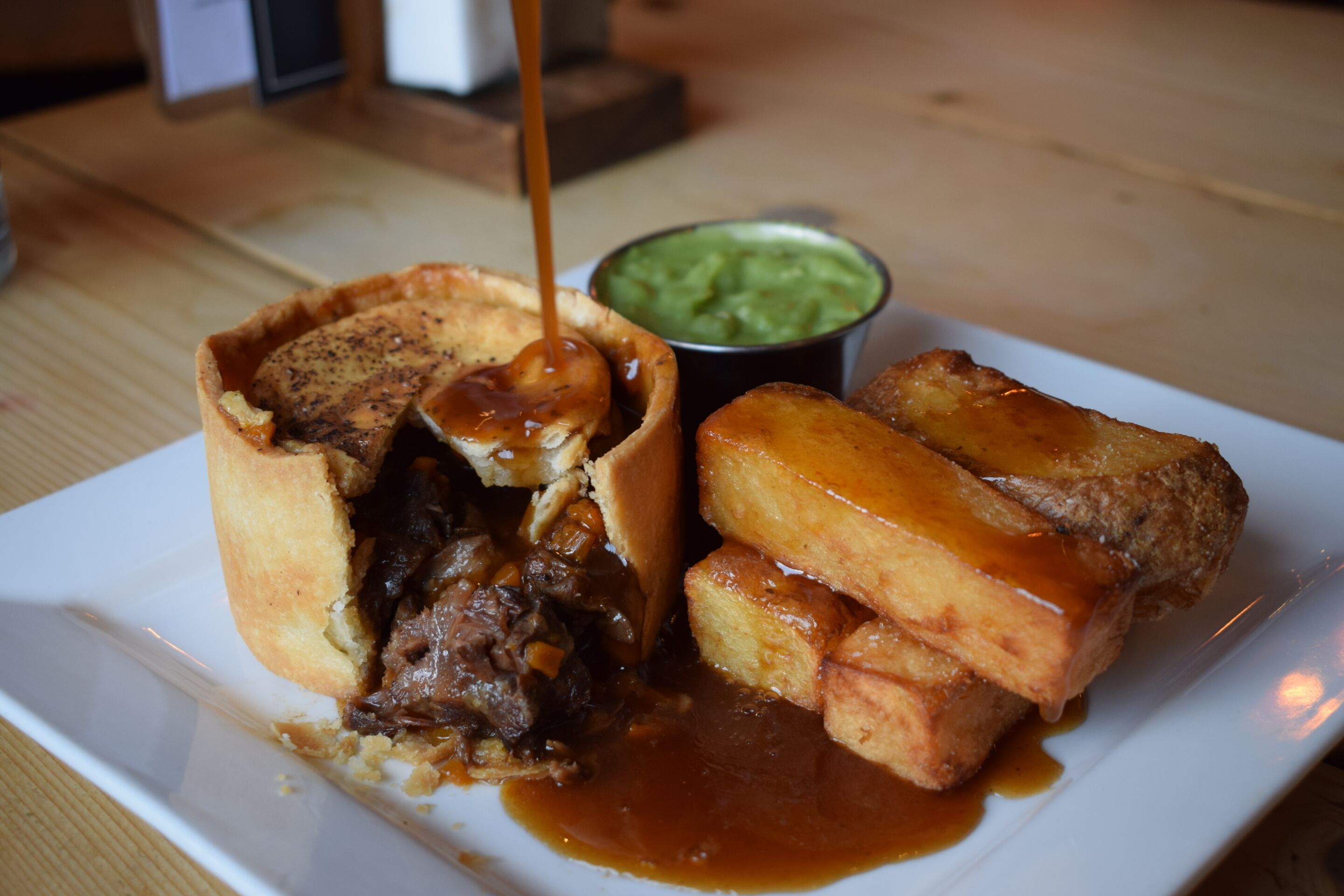 Une assiette contenant un pâté de viande, de la sauce et deux portions de Yorkshire pudding.