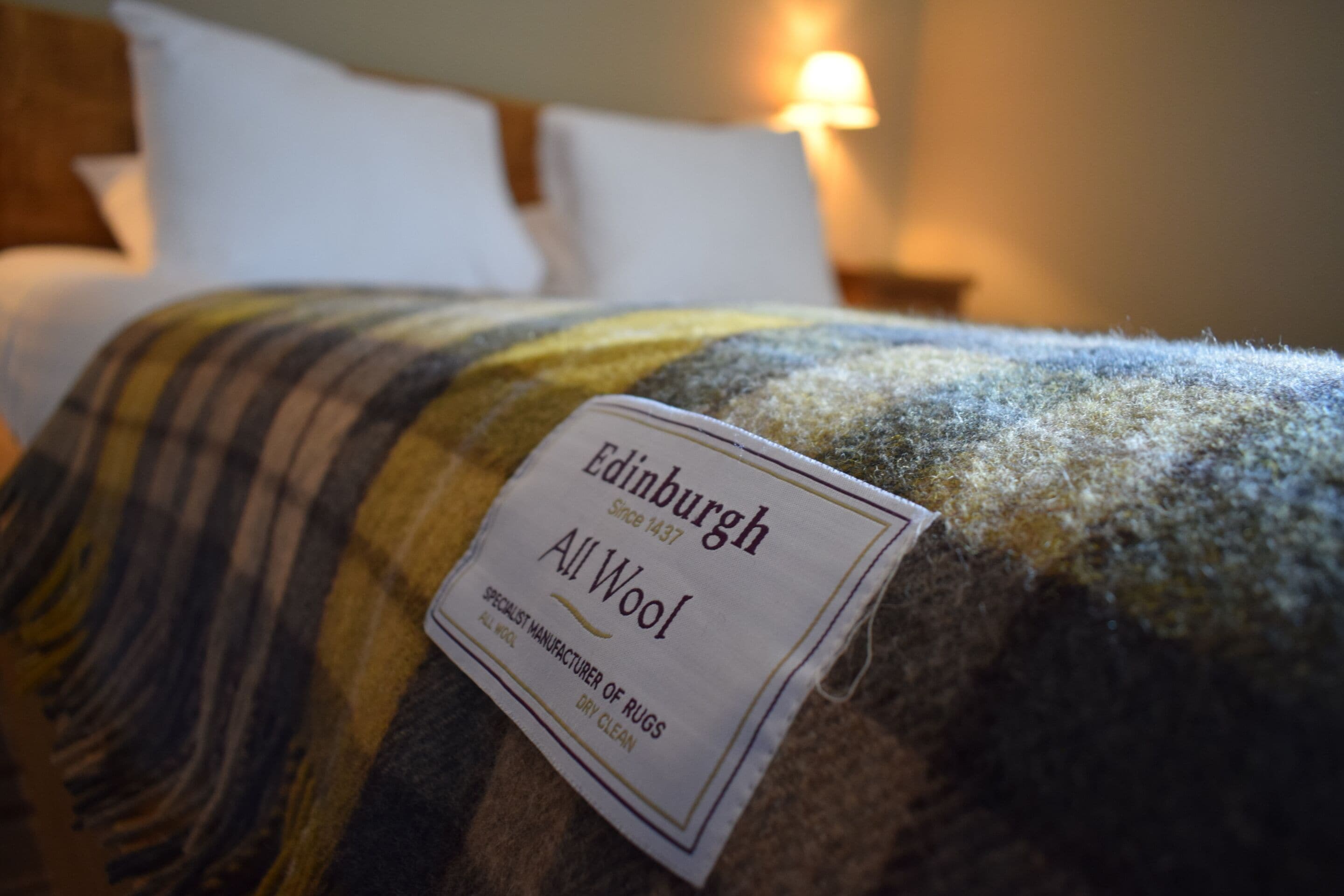 A bed with a tag labeled 'Edinburgh All Wool' indicating the material of the bedding.
