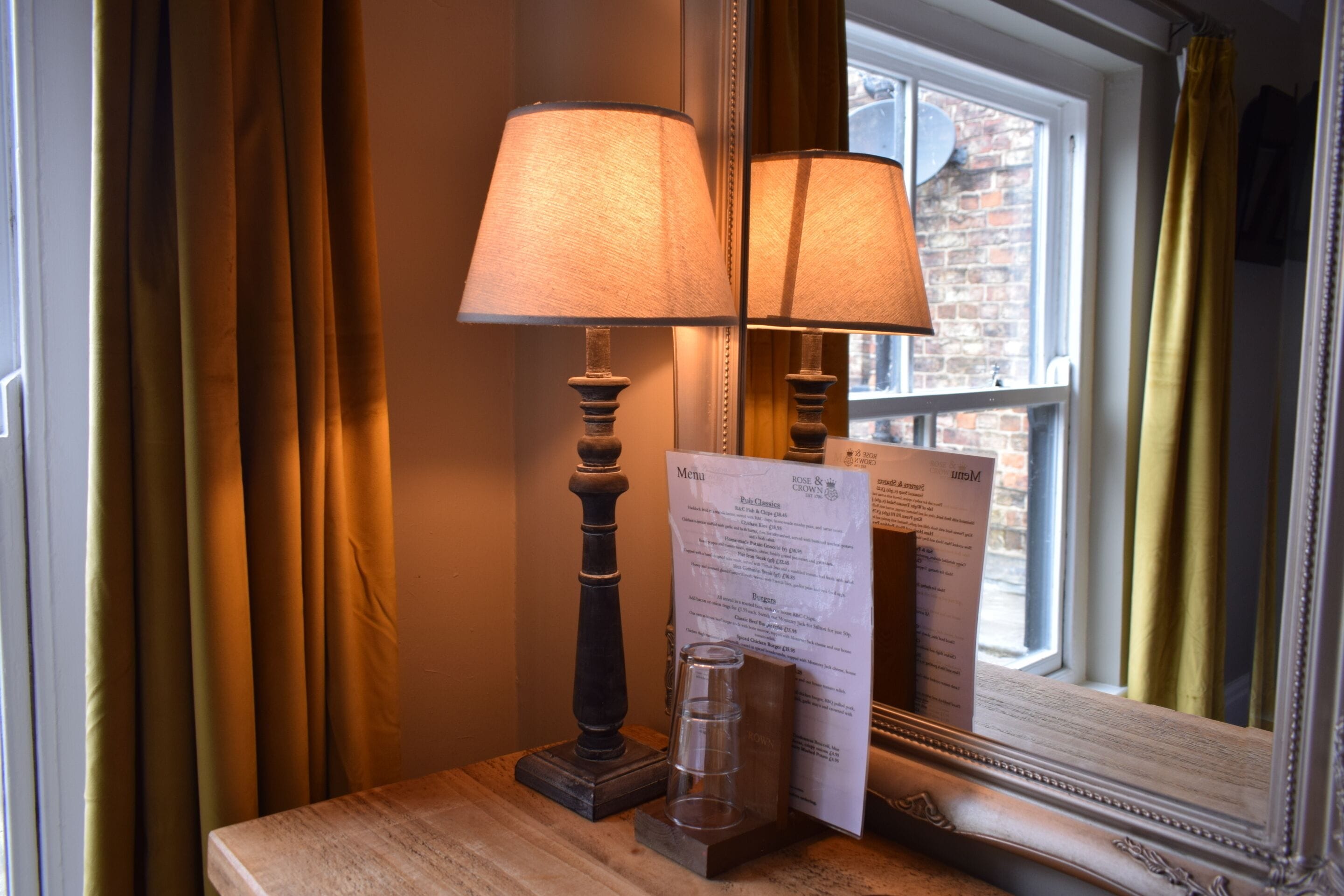 A table with a lamp, a menu, and a glass of water.