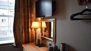 A hotel room with a television mounted above a mirror, a bedside table with a lamp, a kettle, and a cup. - The Rose and Crown (York)