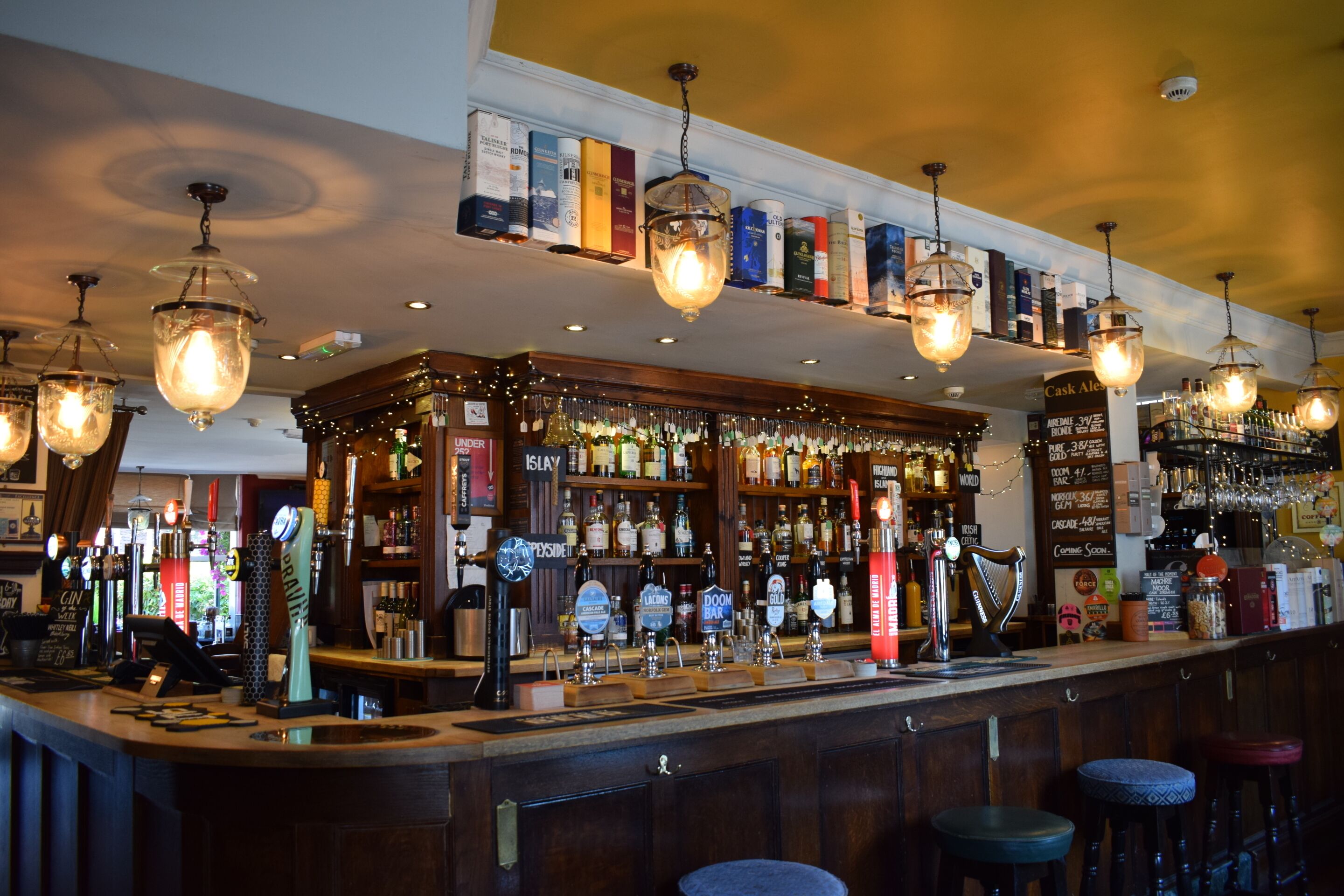 Uma área de bar com várias torneiras de cerveja, prateleiras cheias de garrafas de bebidas e luminárias penduradas.