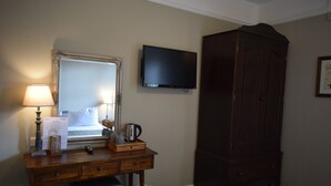 A hotel room with a bed, a desk with a lamp, a television, and a wardrobe.