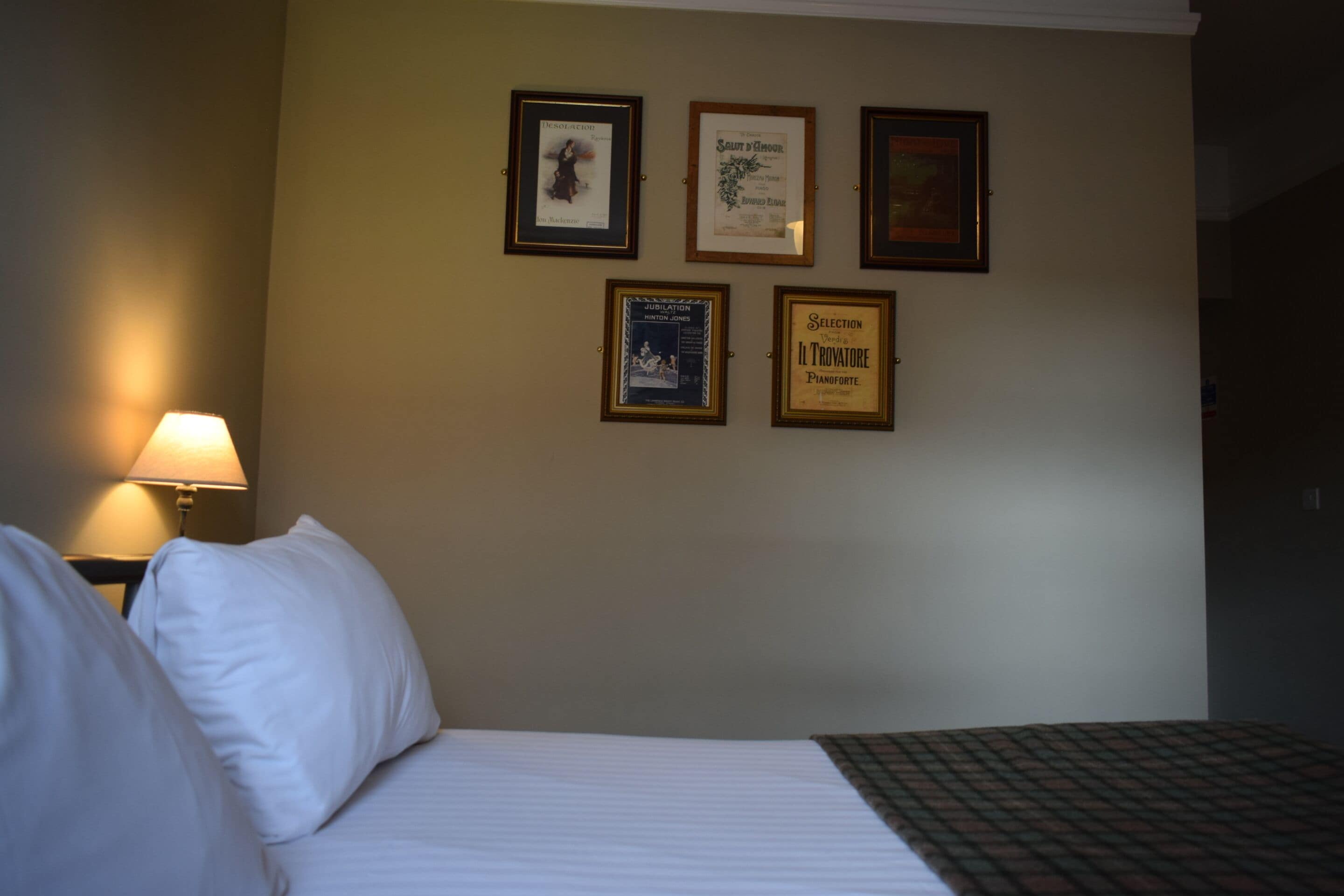 Una habitación de hotel con una cama, una mesita de noche con lámpara y cuatro certificados enmarcados en la pared.