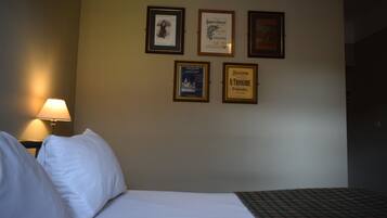 Una habitación de hotel con una cama, una mesita de noche con lámpara y cuatro certificados enmarcados en la pared.
