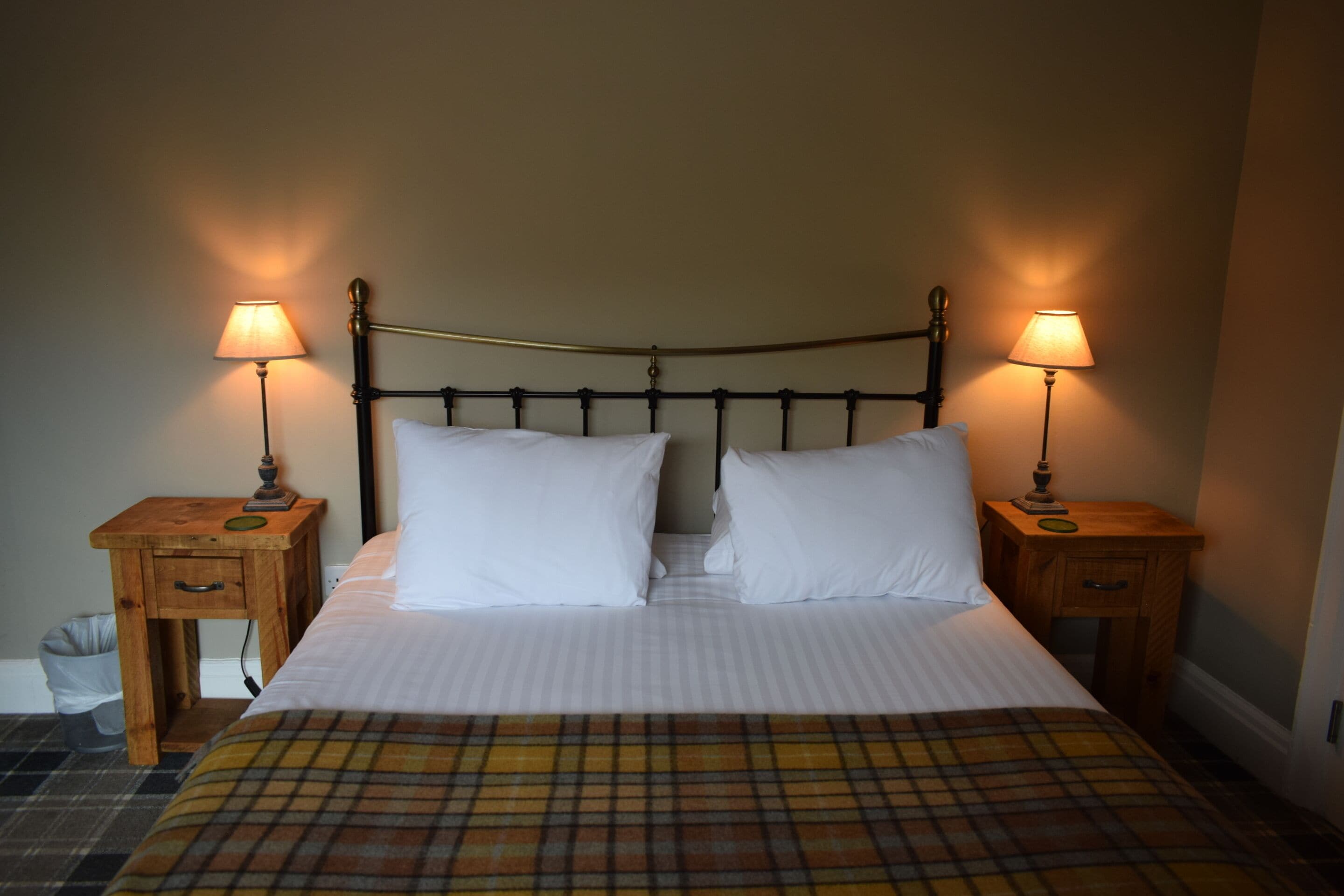 A bed with two white pillows, a plaid blanket, and two bedside tables with lamps.