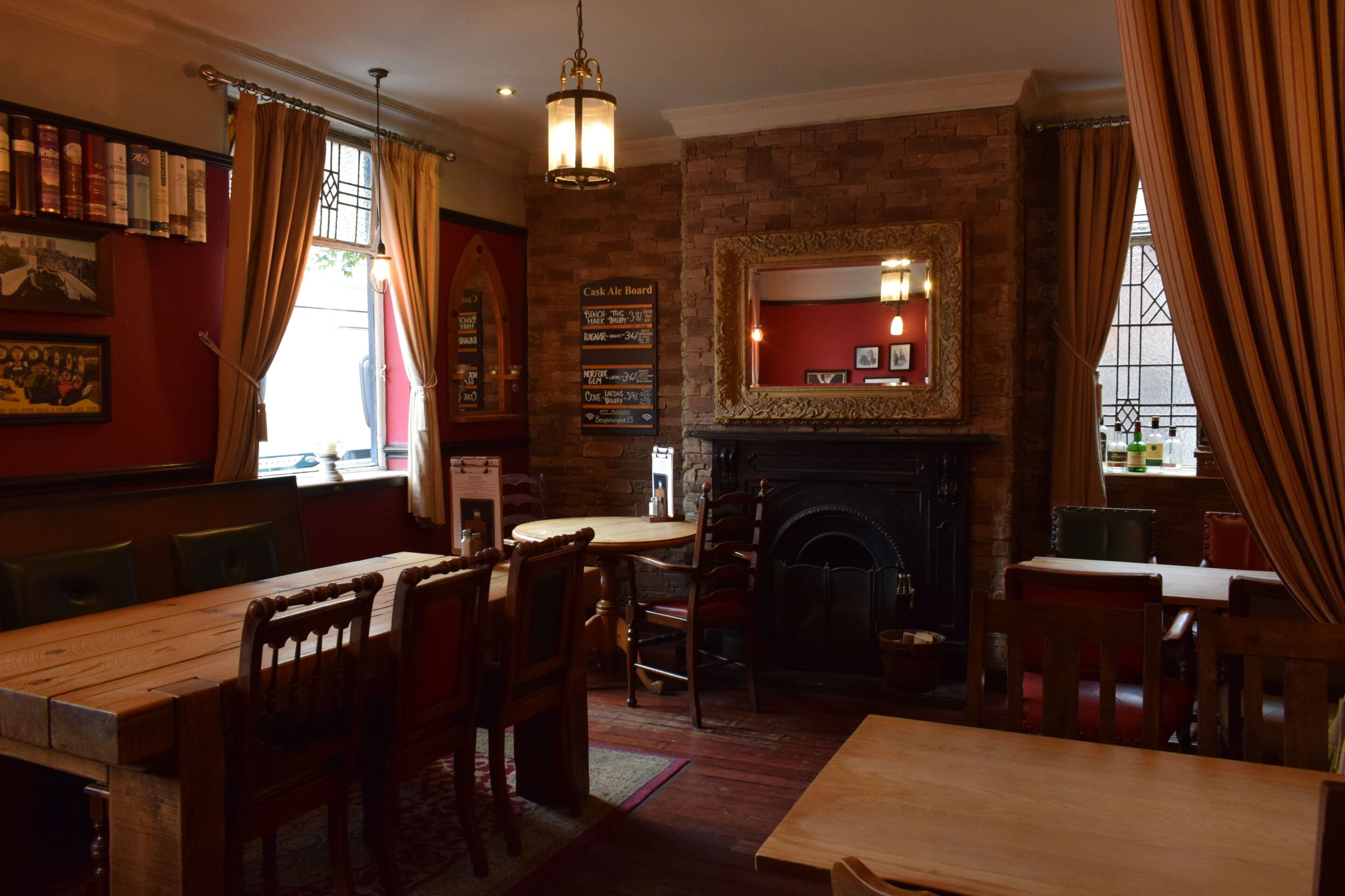 A pub with brick walls, a fireplace, wooden tables and chairs, and a menu board.