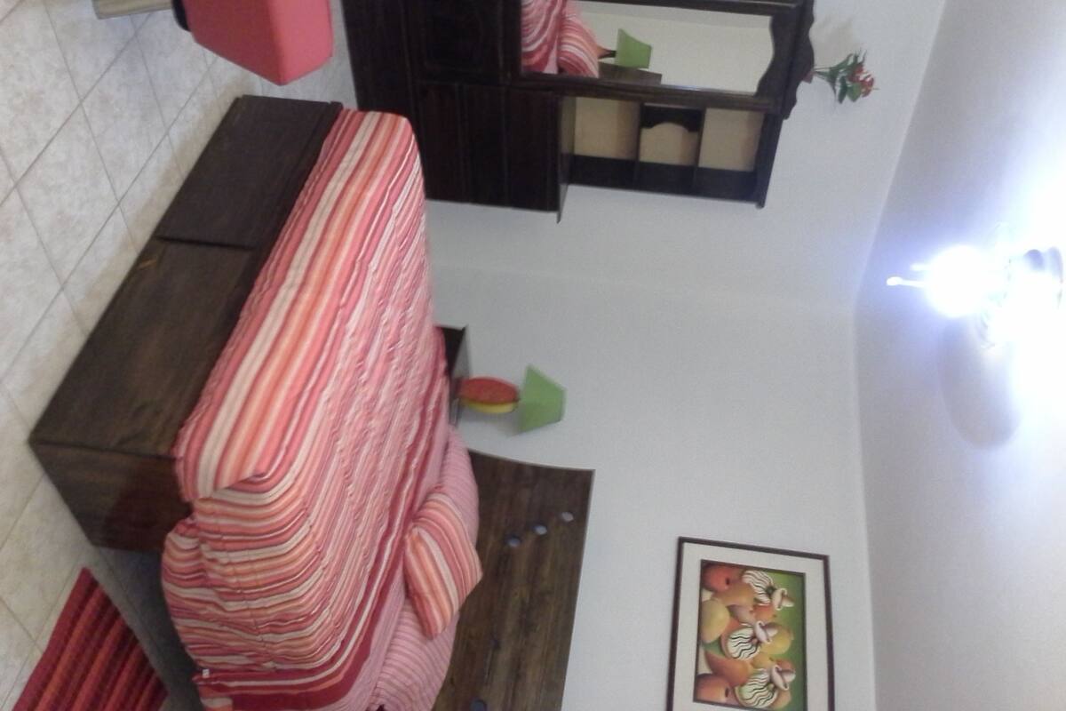 A room with a striped sofa, a small table, a dark wooden cabinet, and a framed picture on the wall.