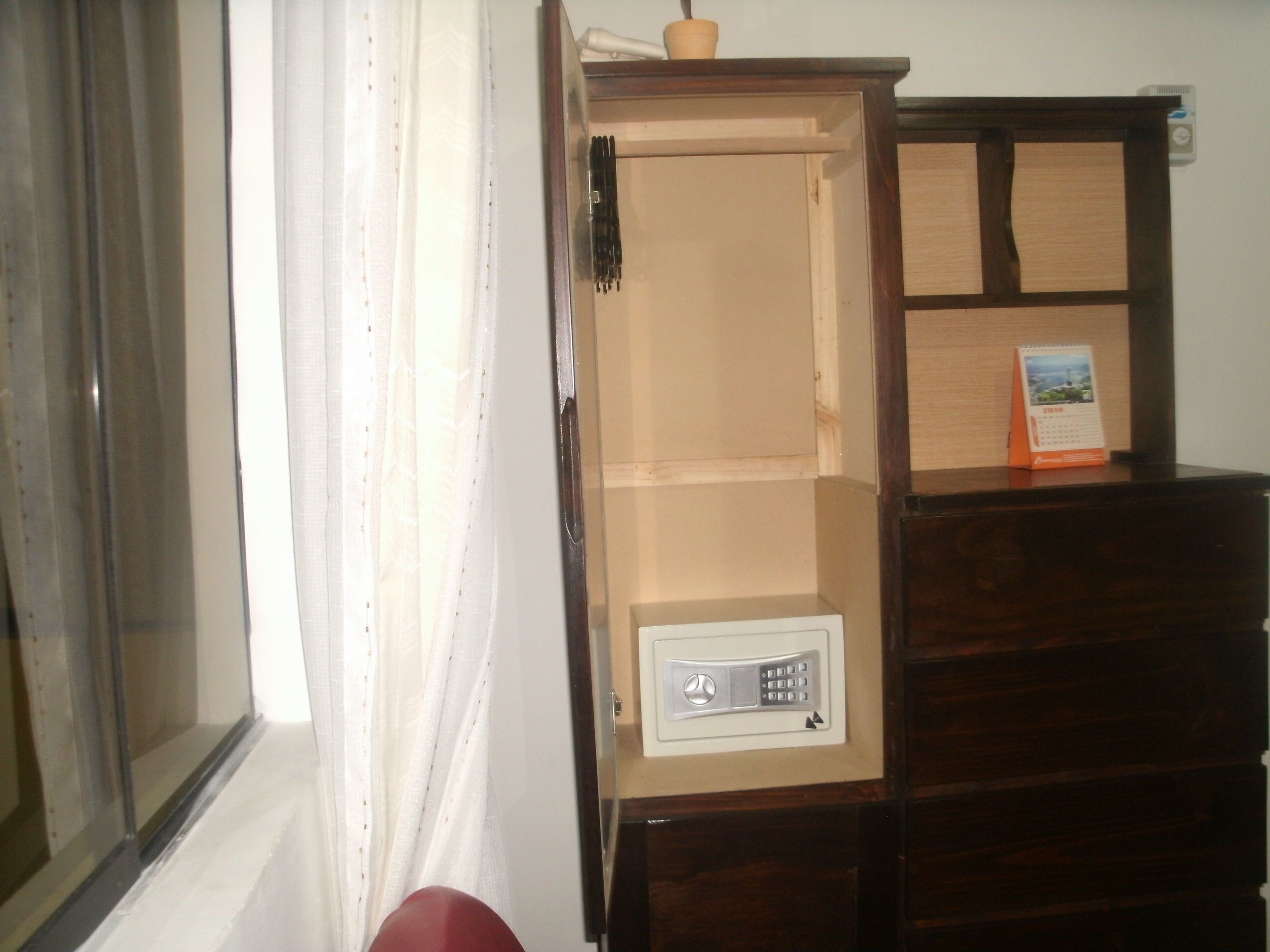 A room with a wooden cabinet, a white wall, and a window with curtains.