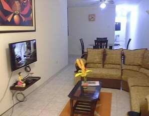 Uma sala de estar com sofá, mesa de centro, televisão e um quadro na parede.