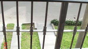 En gelænder af metal på en balkon med udsigt over en belagt plads og græs.