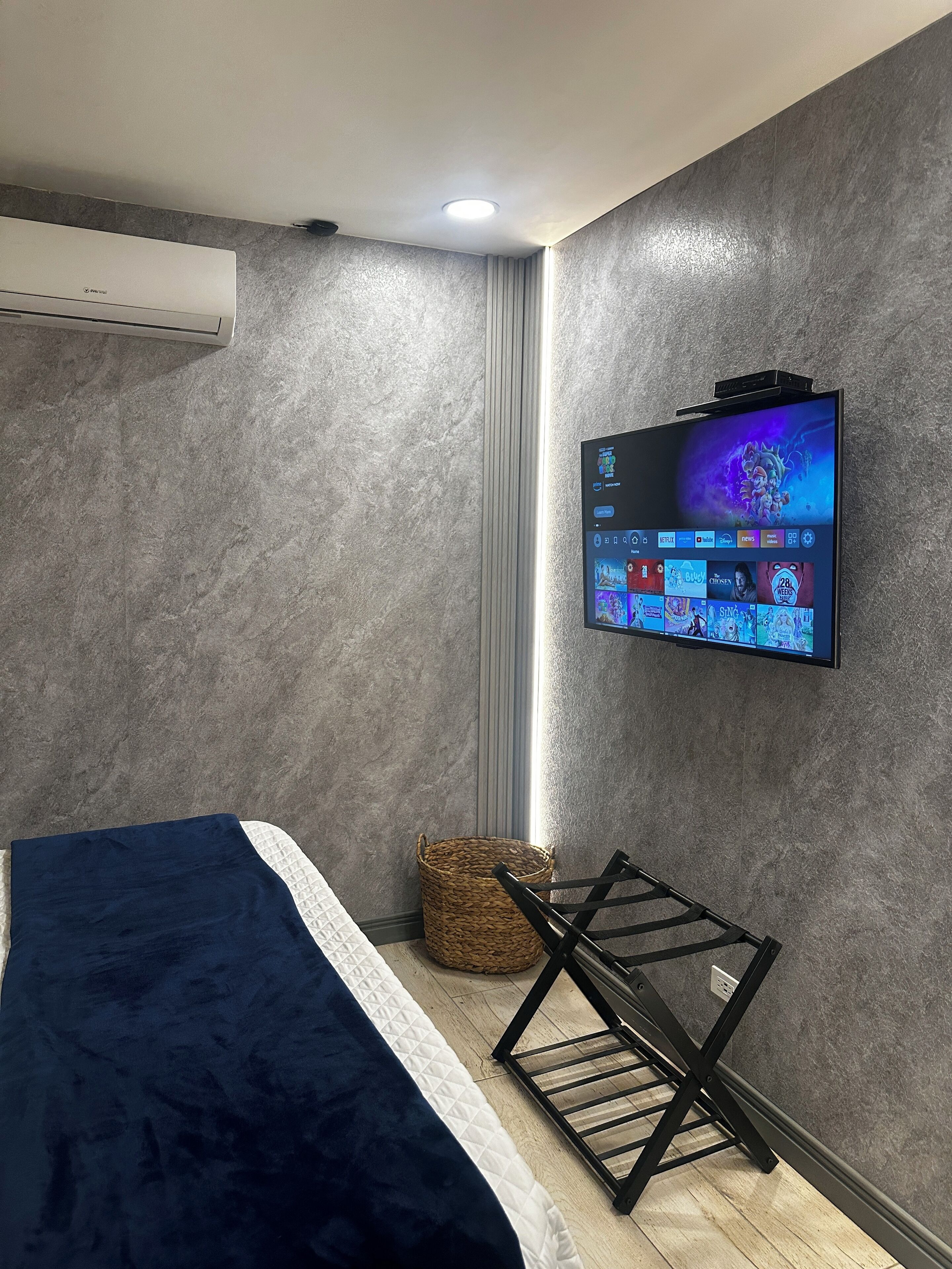 Un dormitorio moderno con cama, televisor montado en la pared y aire acondicionado en el techo.