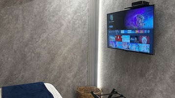 A modern bedroom with a bed, a TV mounted on the wall, and a ceiling air conditioner.