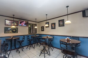 A restaurant interior with multiple tables and chairs, framed pictures on the walls, and hanging pendant lights. - Berlor Airport Inn (Rio Segundo)
