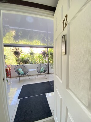 A door with the number 12, leading to a covered outdoor area with two chairs and a small table. - Berlor Airport Inn (Rio Segundo)
