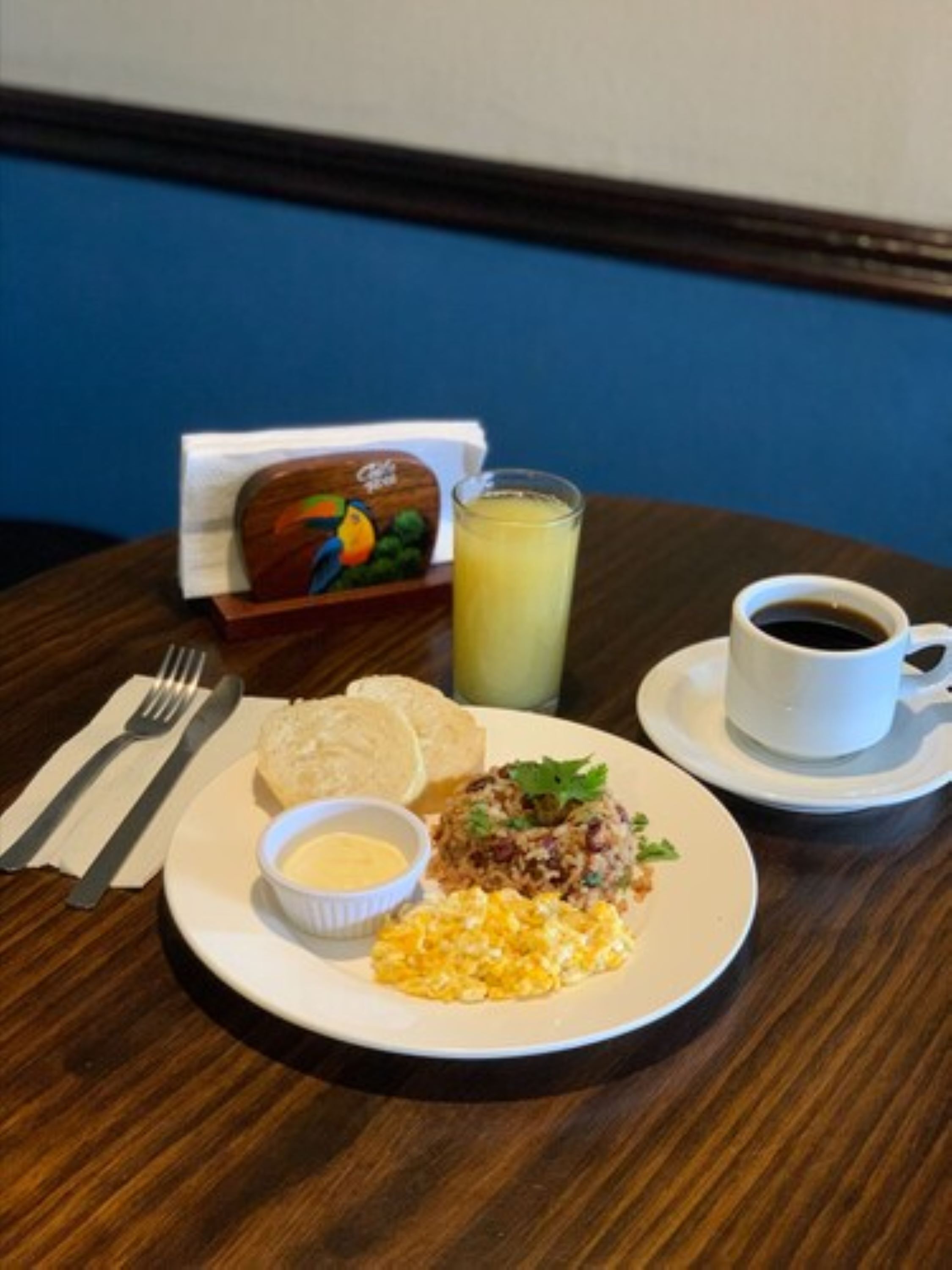 A breakfast plate with scrambled eggs, a meat patty, toast, butter, and a glass of orange juice.