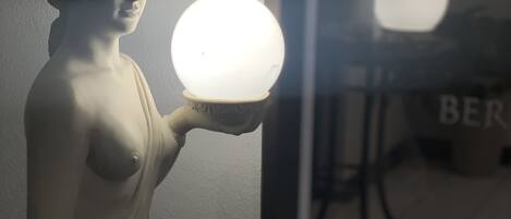 Una estatua de una mujer sosteniendo una bombilla, ubicada junto a un espejo que refleja una silla y una pared con la palabra "BER".