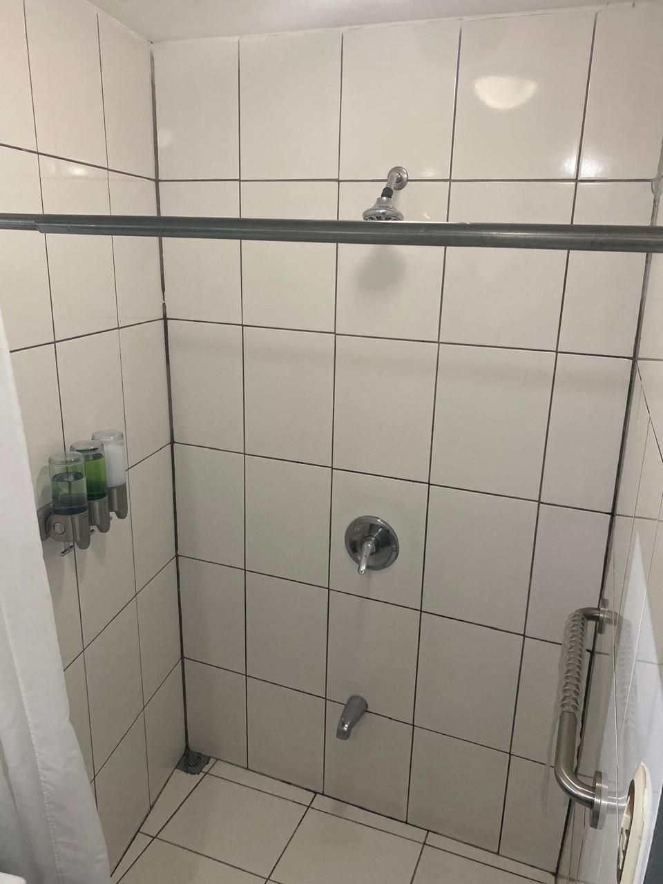 Un vestuario de ducha pequeño con azulejos, un cabezal de ducha de mano, un grifo empotrado y una puerta de cristal.