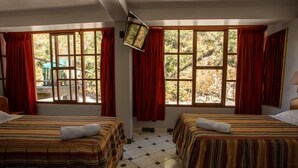 A hotel room with two beds, large windows with red curtains, a tiled floor, and a television mounted on the wall. - Hostal La Payacha (Machu Picchu)