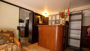 A compact living space with a wooden reception desk, a cushioned chair, and a refrigerator. - Hostal La Payacha (Machu Picchu)
