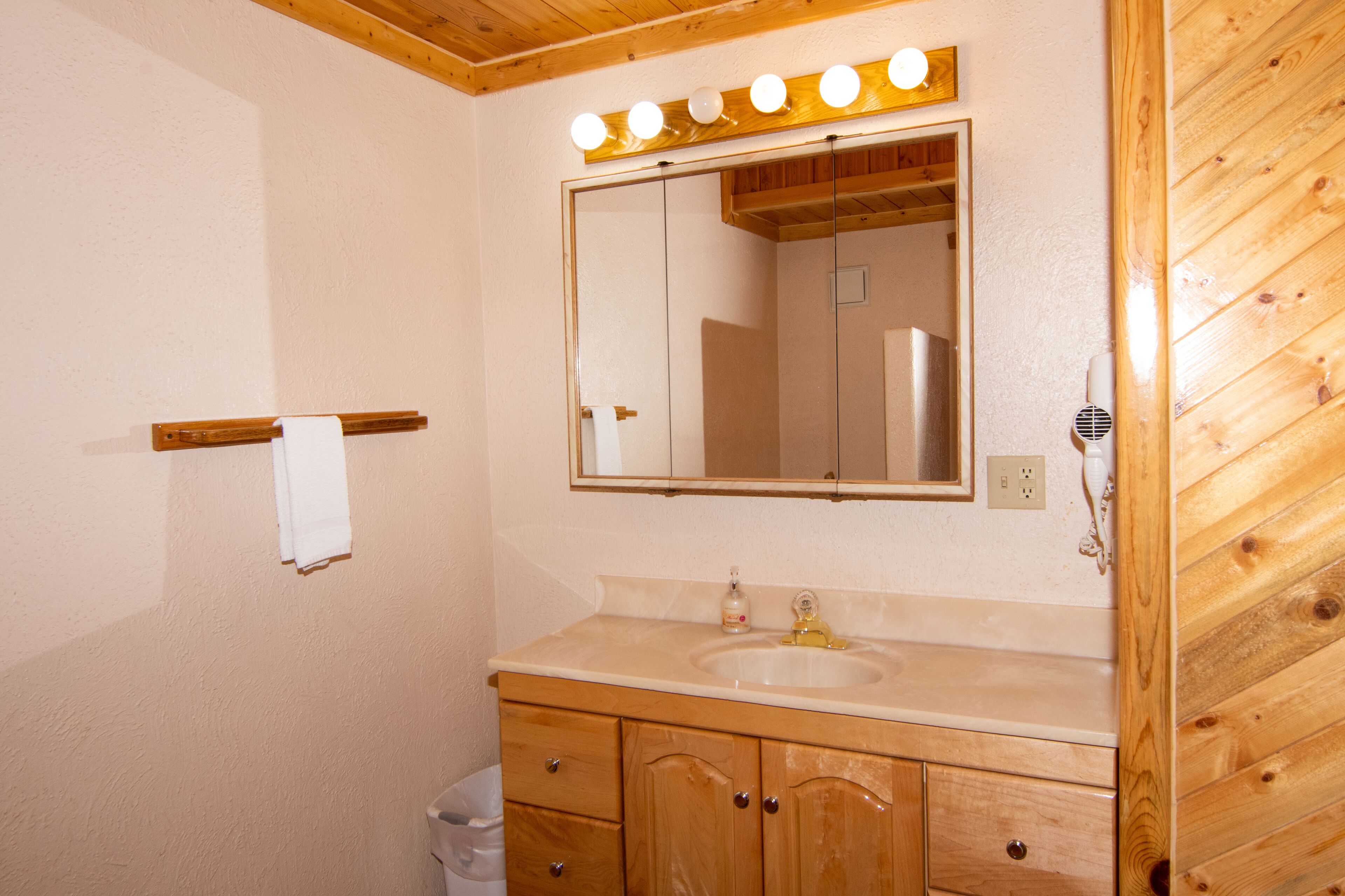 Une salle de bain avec des meubles en bois, un lavabo et un miroir surmonté de luminaires.